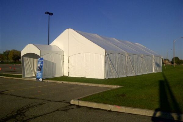 30’x60’ Legacy Tent Structure with a solid white roof, solid white walls, staked into the ground used as for a corporate training/leadership event. A 10’ wide Legacy LT tent is set out front as a check in space.